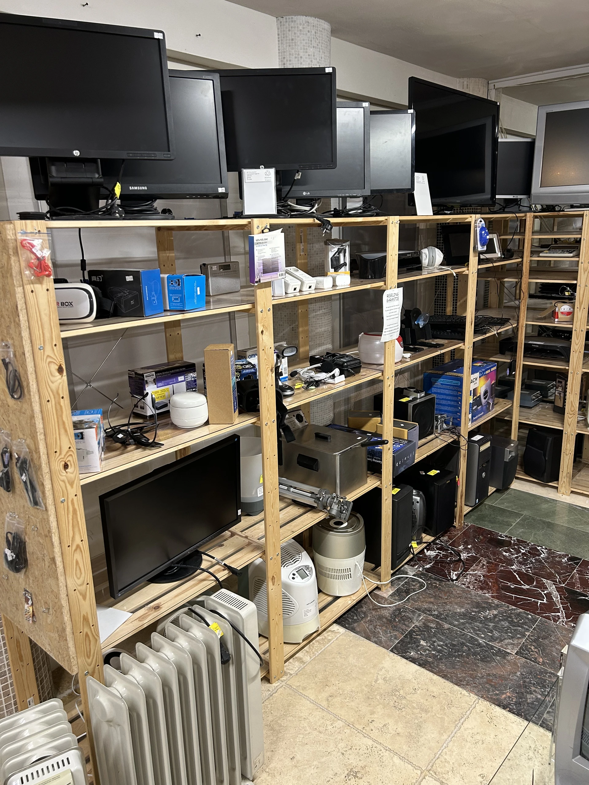 Houten stellingen met elektronica, computers en huishoudelijke apparaten in een kringloopwinkel