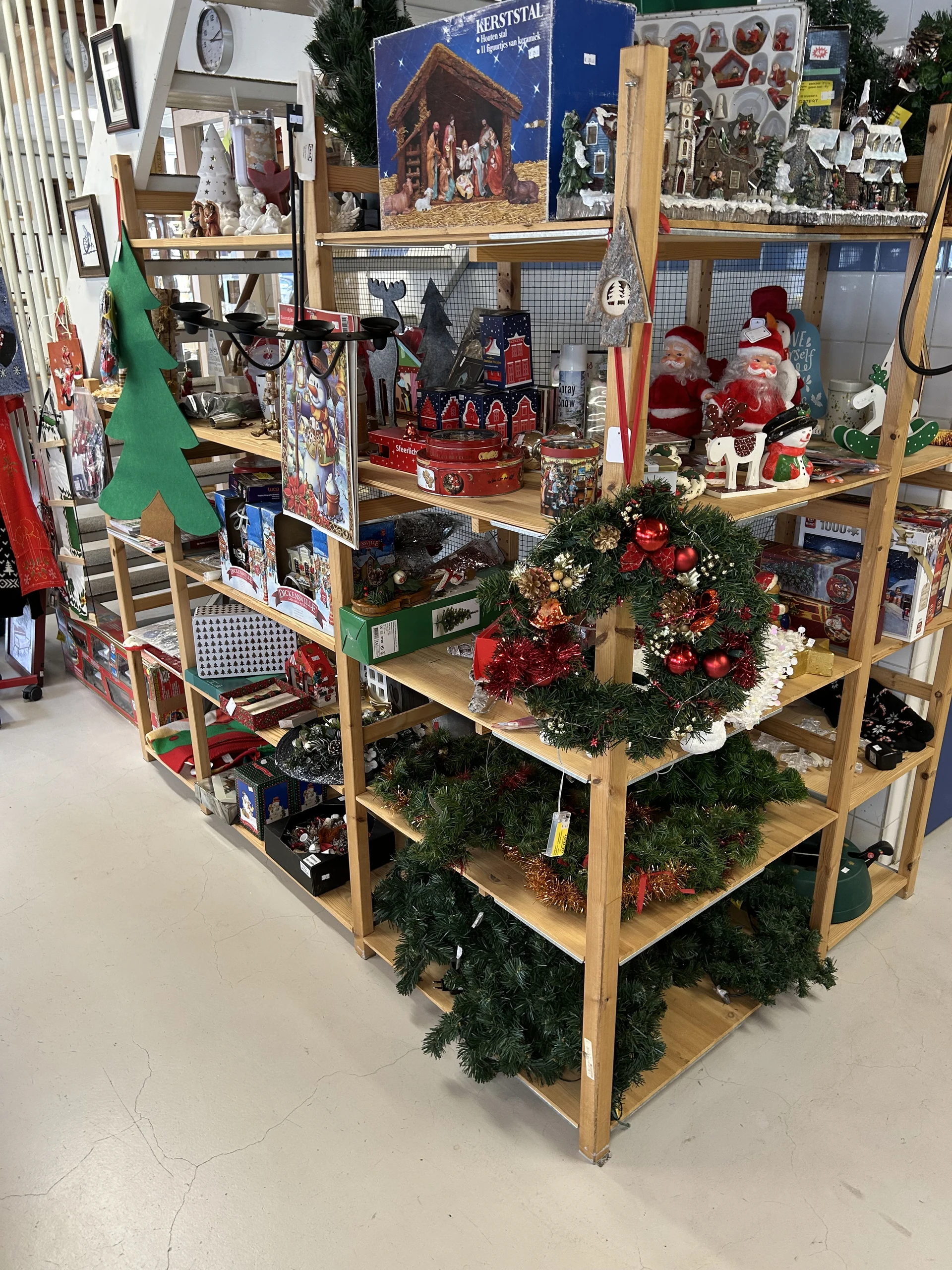 Houten display met kerstdecoraties, waaronder kerstkransen, kerstmannen en rode kerstballen