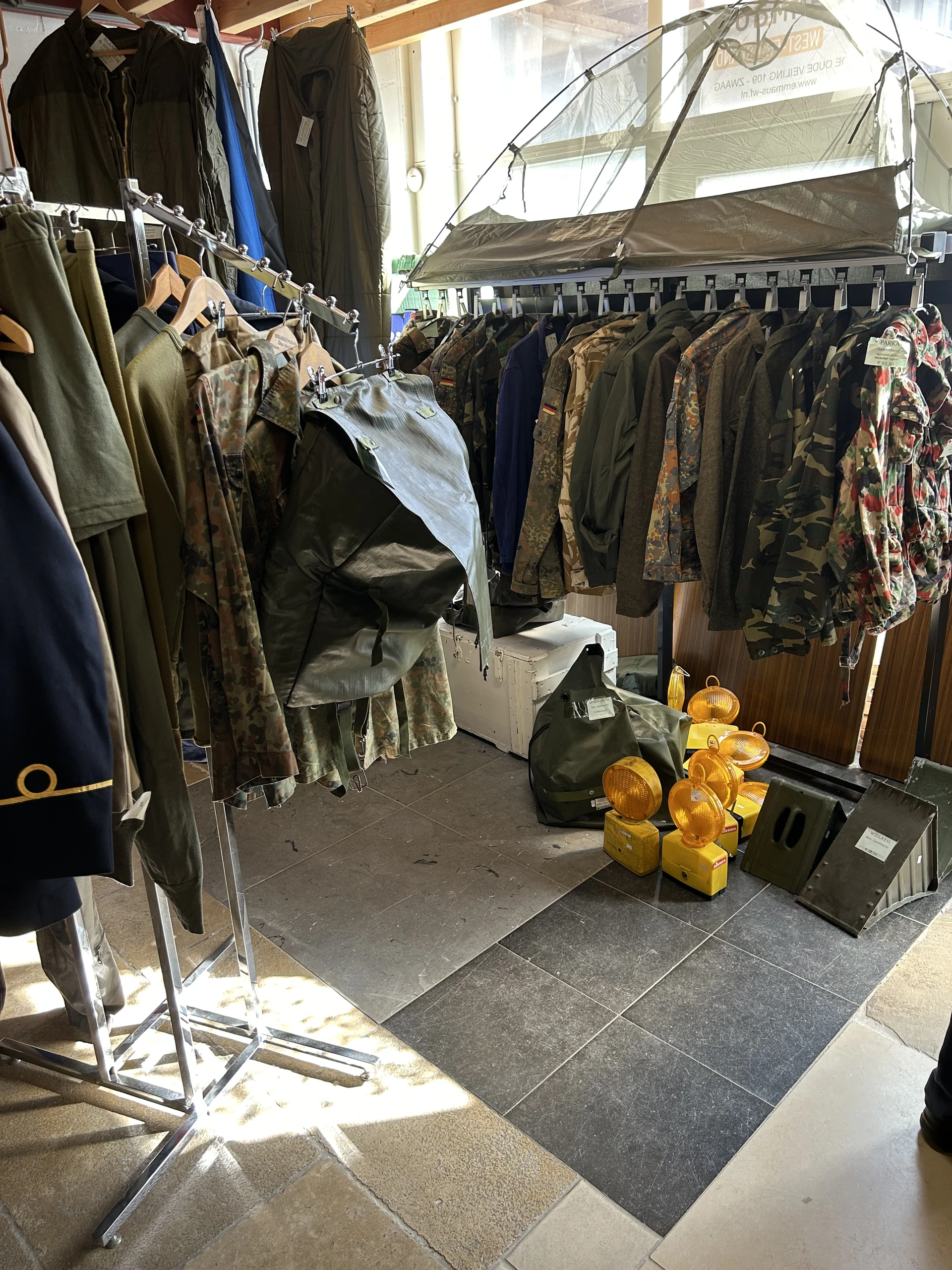 Kledingrekken met jassen en vintage kleding in een kringloopwinkel, met gele lampen op de grond