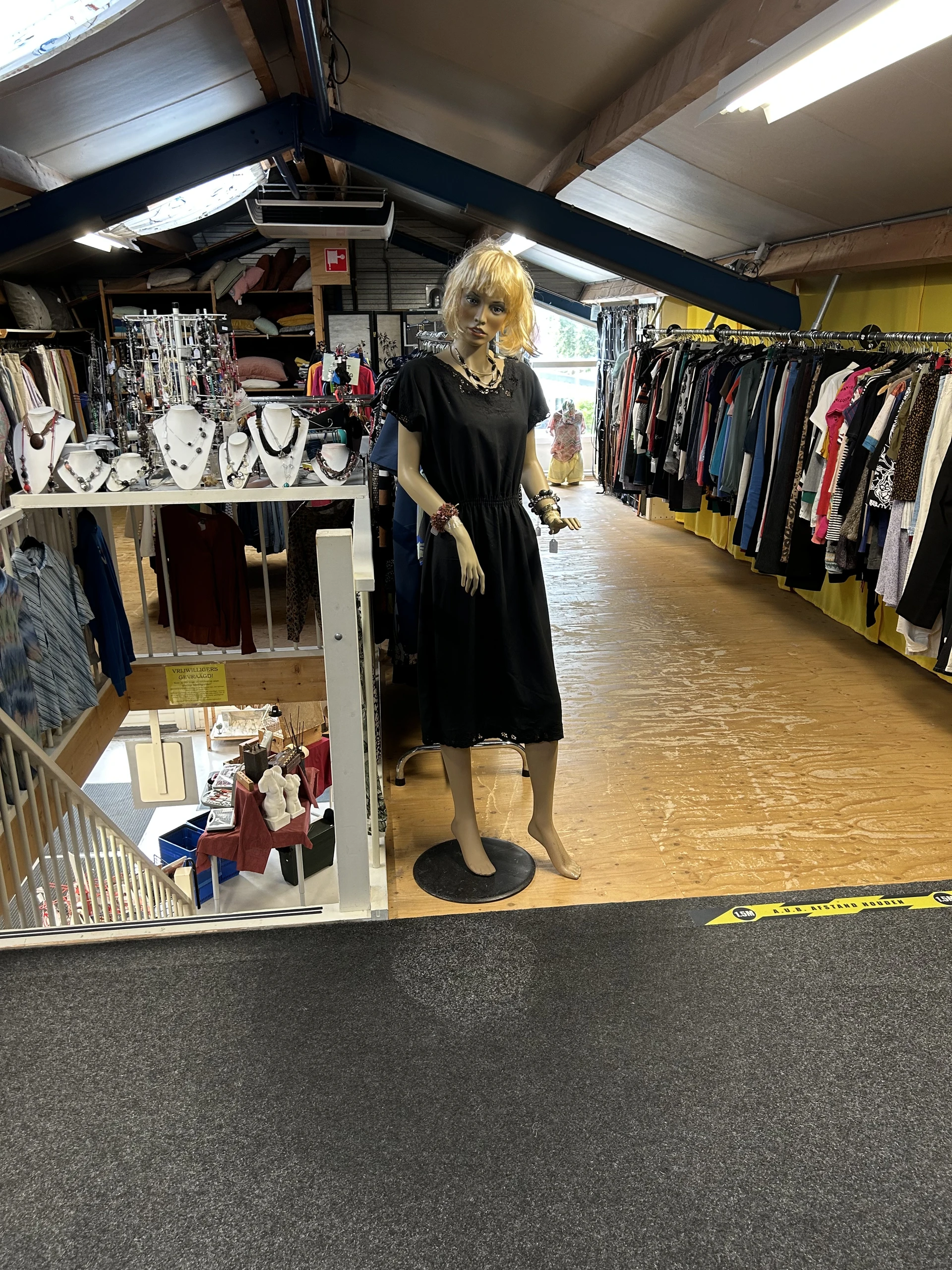 Interieur van kringloopwinkel met kledingrekken, etalagepop in zwarte jurk, sieradendisplay en diverse tweedehands artikelen