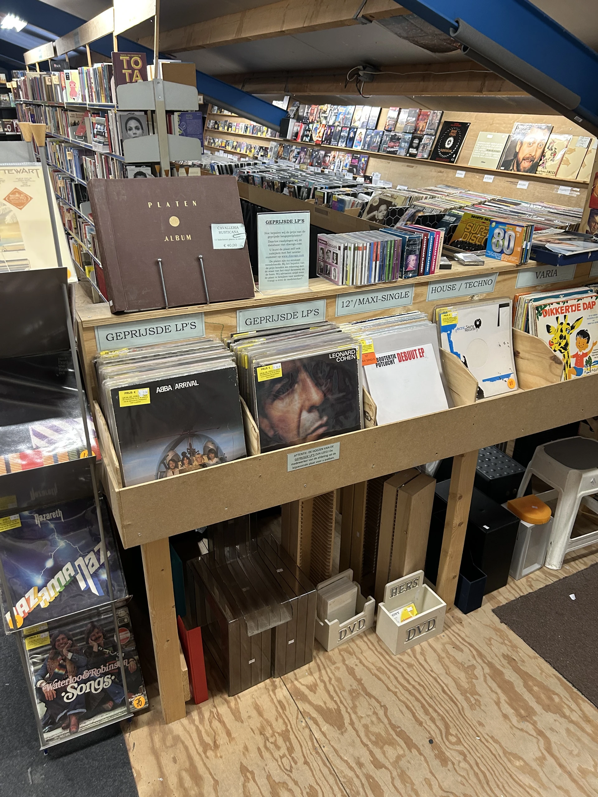 Houten stellingen met uitgestalde vinyl platen, cd's en ander muziekmateriaal in een kringloopwinkel