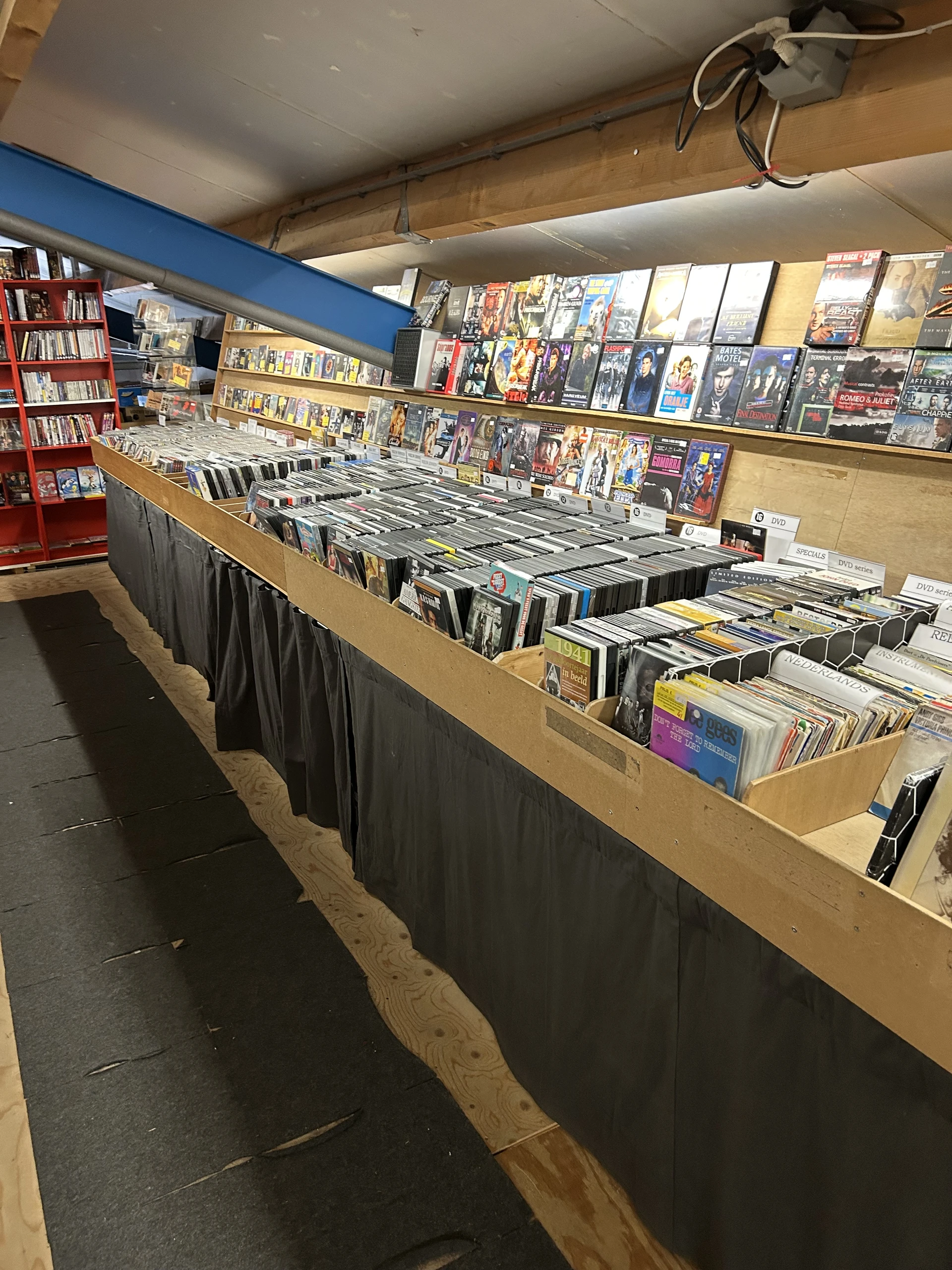 Lange tafel met uitgestalde cd's, dvd's en andere media in rekken, op de achtergrond boekenkasten