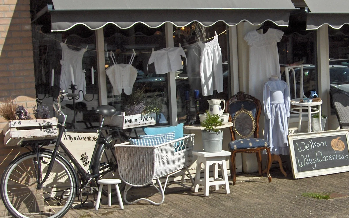 Winkelvoorgevel met luifel en uitstallingen met kleding, fiets en huisraad