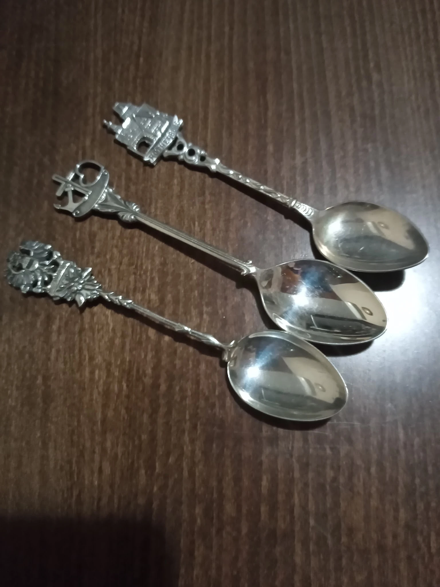 Drie zilveren theelepels met decoratieve handvatten op houten ondergrond