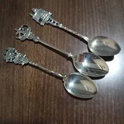 Drie zilveren theelepels met decoratieve handvatten op houten ondergrond