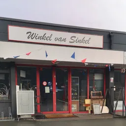 Voorgevel van kringloopwinkel Winkel van Sinkel met rode deuren, zwart frame en gekleurde vlaggetjes, diverse artikelen zicht