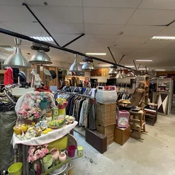 Winkelvloer met kledingrekken, tafels met decoratiespullen en grote ventilators aan het plafond