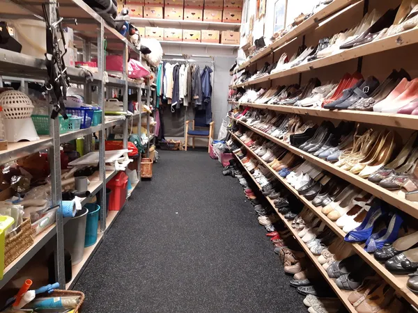 Winkelinterieur met schoenrekken langs de wand en kleding aan hangers achter in de winkel