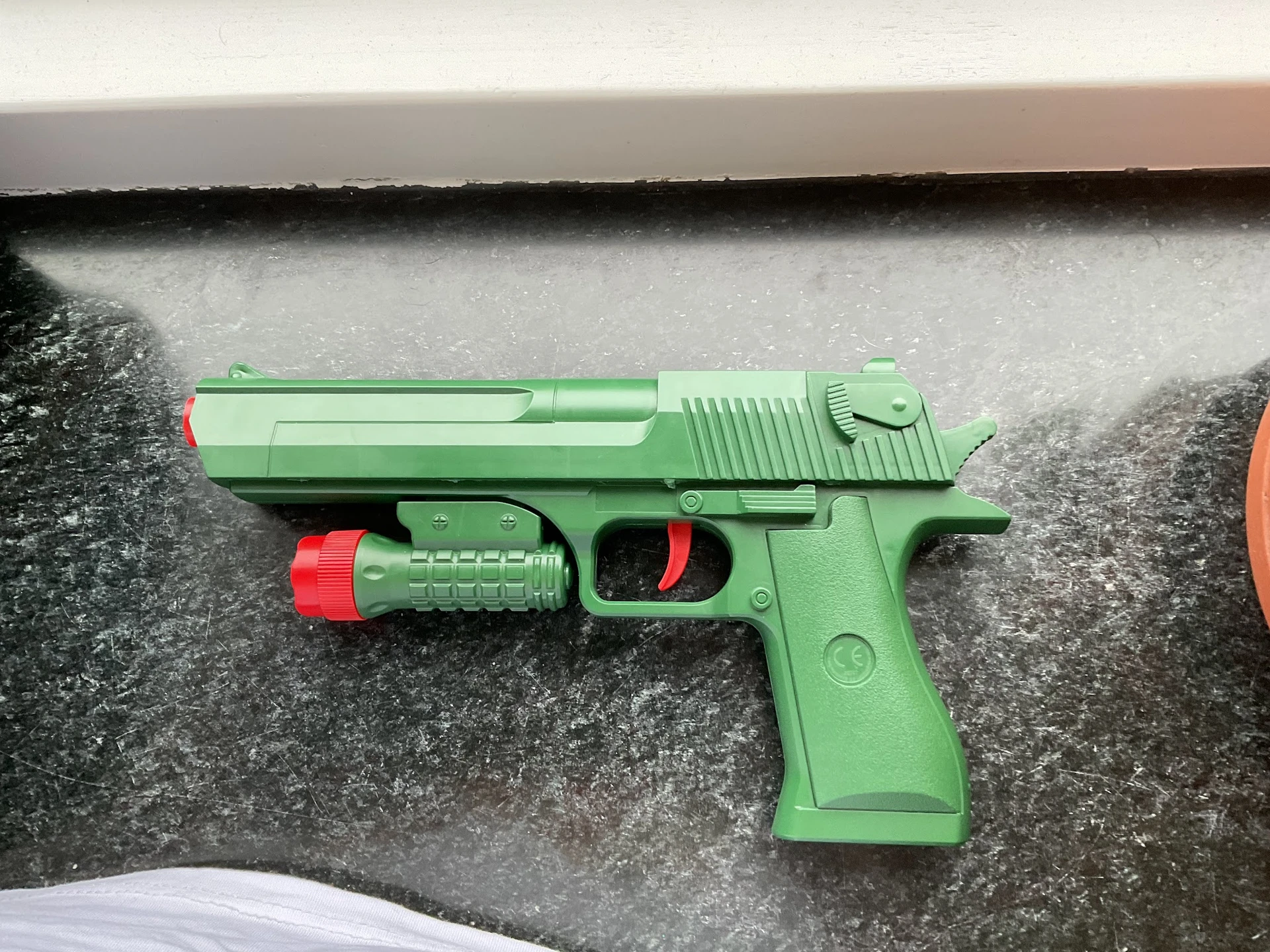 Groen speelgoedpistool met rode details op betonnen ondergrond