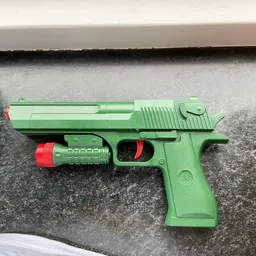 Groen speelgoedpistool met rode details op betonnen ondergrond