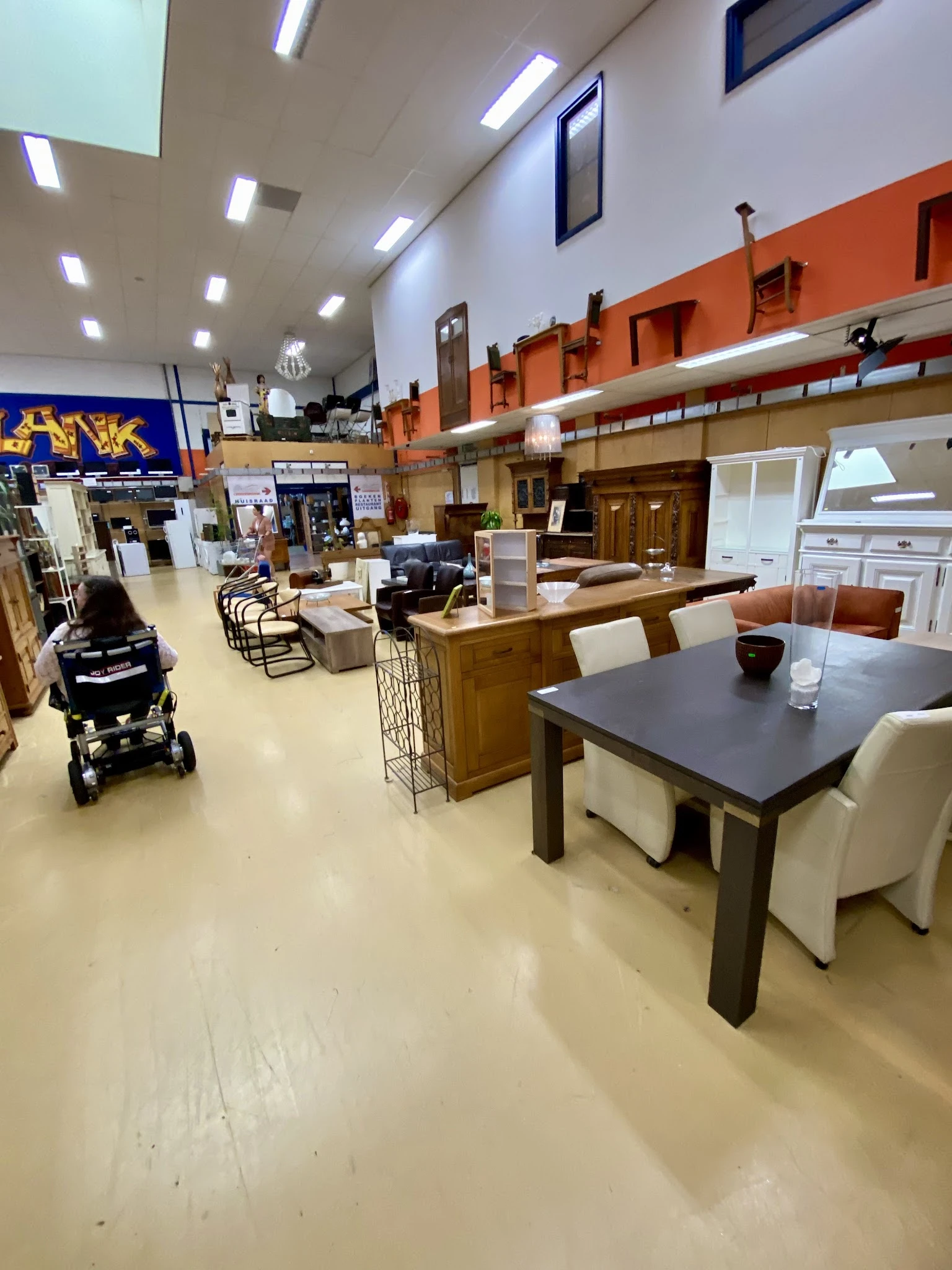 Woonwarenwinkel met houten tafels, stoelen en kasten uitgestald in een groot open interieur met oranje accenten