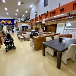 Woonwarenwinkel met houten tafels, stoelen en kasten uitgestald in een groot open interieur met oranje accenten