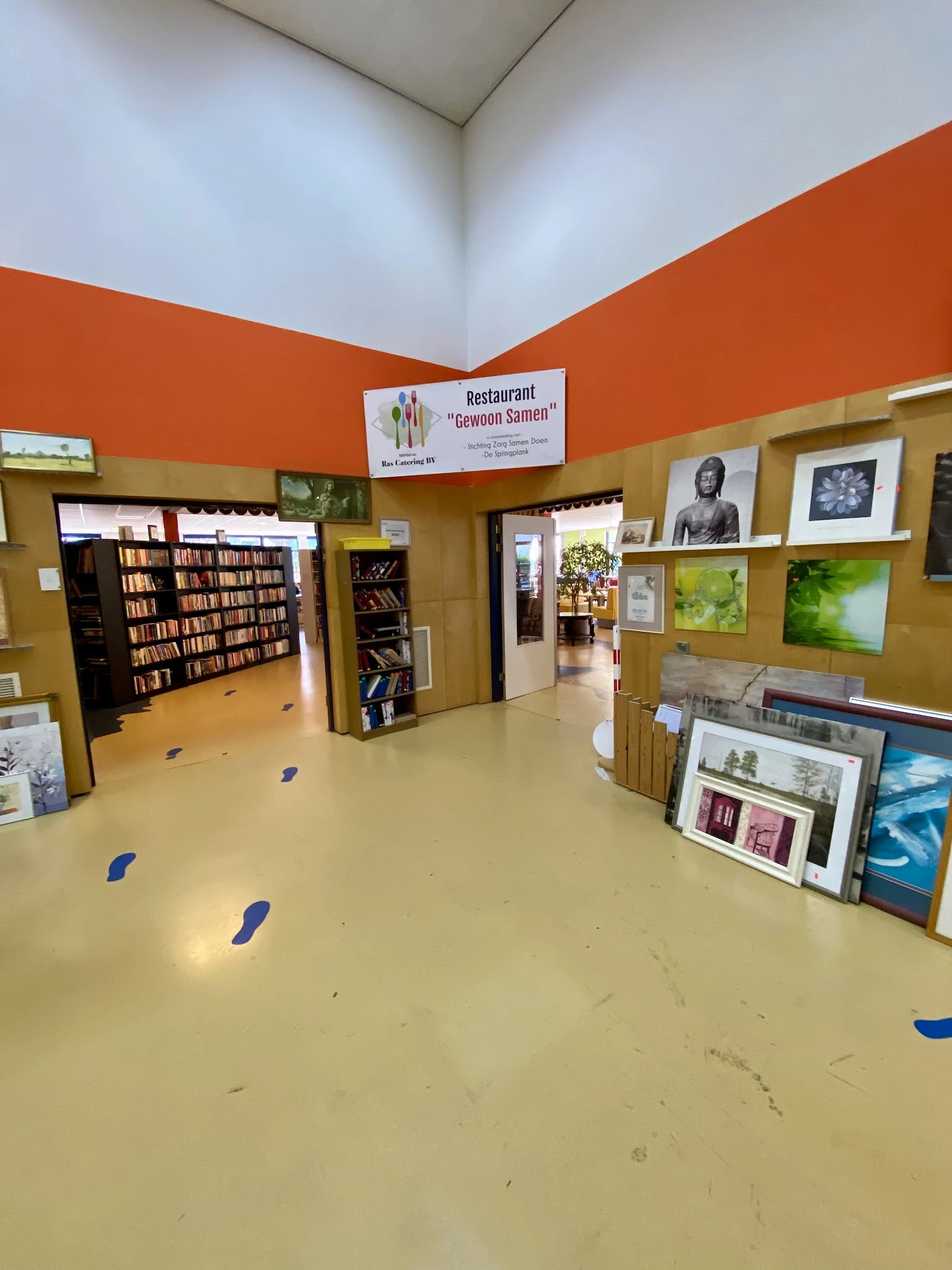 Winkelvloer met boekenkasten, kunstwerken aan muren en diverse spullen in een kringloopwinkel
