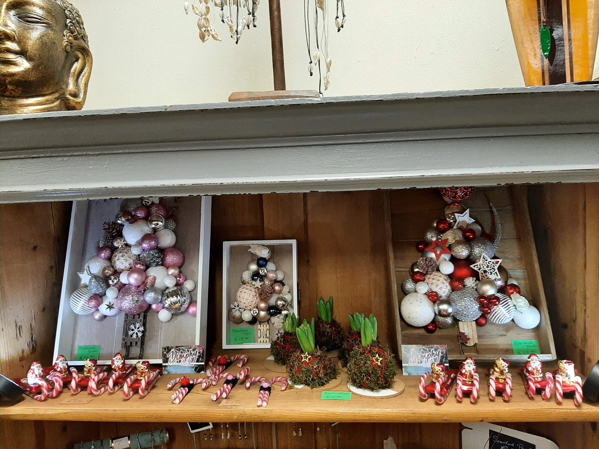Vitrinekast met kerstdecoraties: glazen ballen, figuren en roze/rode ornamenten