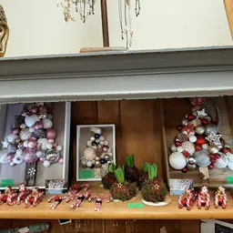Vitrinekast met kerstdecoraties: glazen ballen, figuren en roze/rode ornamenten
