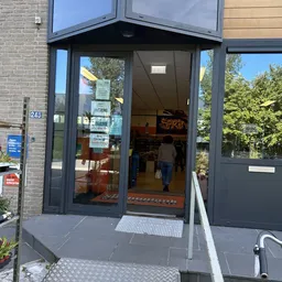 Glazen winkelpui van kringloopwinkel met donkergrijze ramen en deur, winkelnémmer 248 zichtbaar, enkele bezoekers binnen