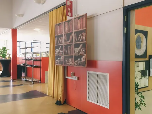Winkelvloer met rode en witte wanden, gele gordijnen, boekenrek en plantenbak in kringloopwinkel