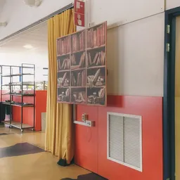 Winkelvloer met rode en witte wanden, gele gordijnen, boekenrek en plantenbak in kringloopwinkel