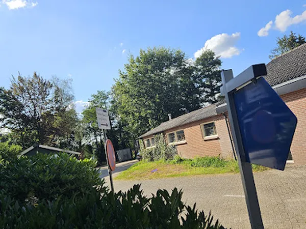 Voorgevel van bakstenen kringloopwinkel met toegangsweg, mailbox en tuin