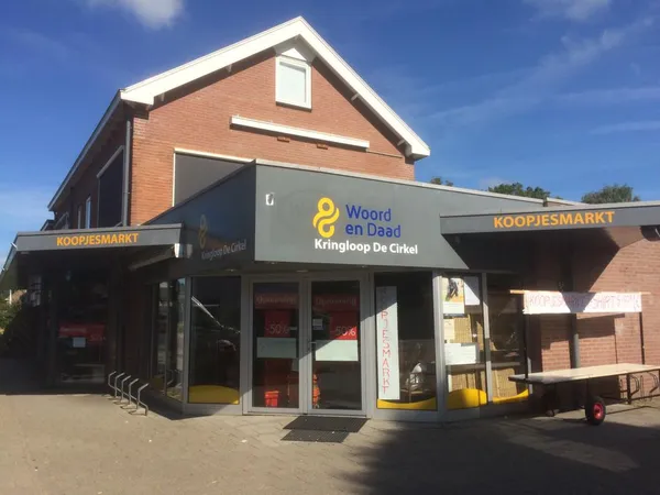 Voorgevel van kringloopwinkel Woord en Daad - Kringloop De Cirkel met winkelname zichtbaar op donkere gevel