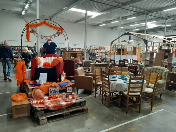 Winkelvloer met uitgestalde meubels, een oranje Halloween-display en bezoekers in een kringloopwinkel