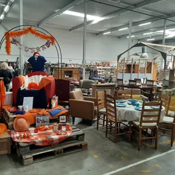Winkelvloer met uitgestalde meubels, een oranje Halloween-display en bezoekers in een kringloopwinkel