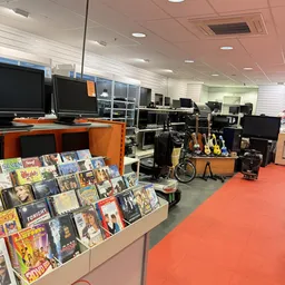 Kringloopwinkelinterieur met computermonitoren, oranje meubels, muziekinstrumenten en dvd's aan het raam