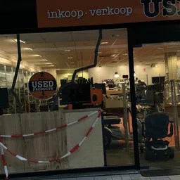 Winkelinterieur met gesloten deur, rood-wit lint, kinderwagens en diversen huishoudartikelen op rekken