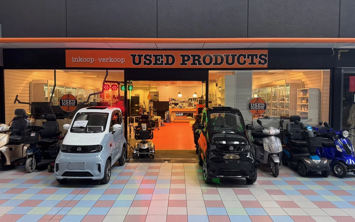 Voorgevel van Used Products kringloopwinkel met oranje entree, uitgestalde auto's en scooters ervoor
