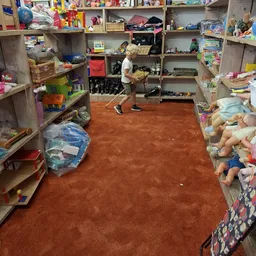 Winkelvloer met speelgoed en kinderartikelen op stellingen aan weerszijden, kind in het midden