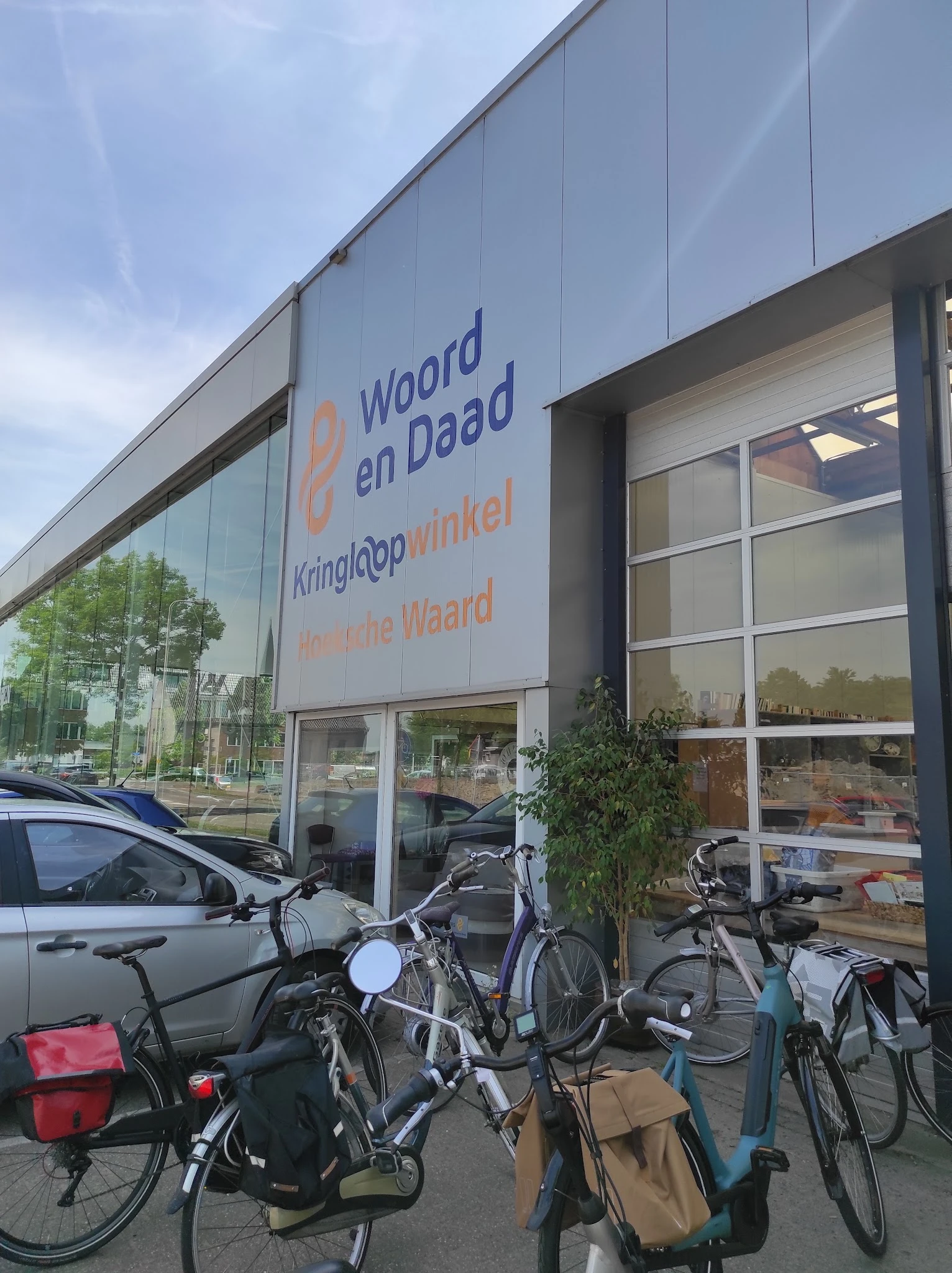 Gevel van kringloopwinkel met grote ramen, winkelnaam op signage, fietsen buiten, straatview