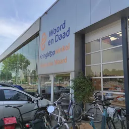 Gevel van kringloopwinkel met grote ramen, winkelnaam op signage, fietsen buiten, straatview