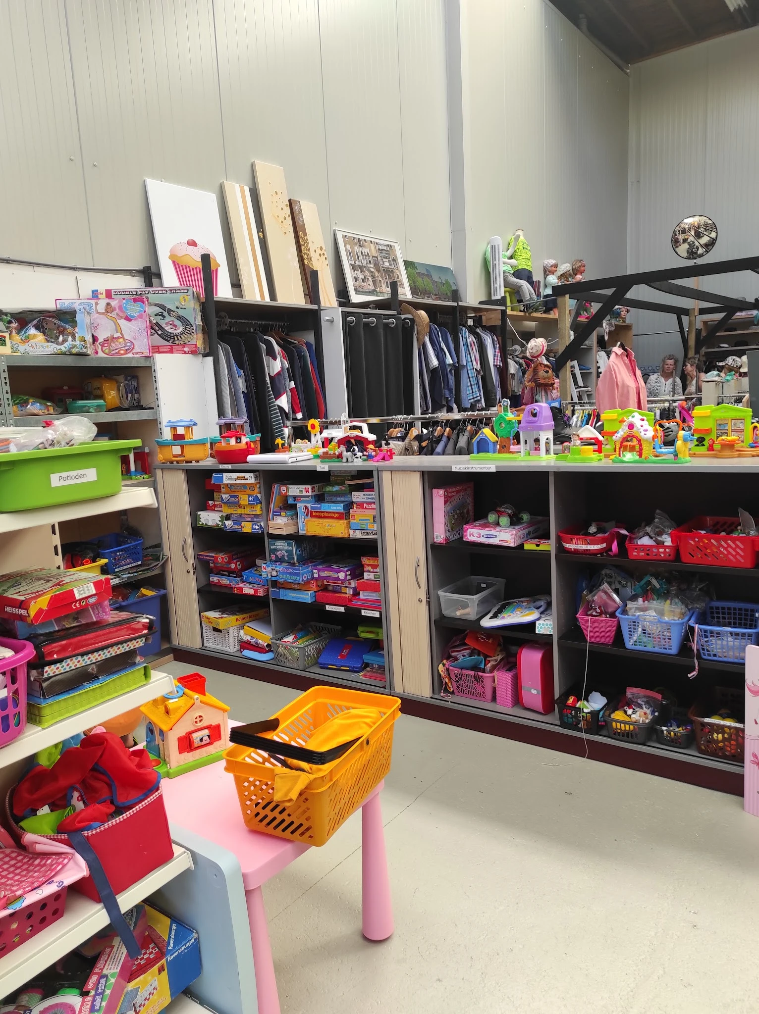 Speelgoedafdeling in kringloopwinkel met dozen, bakjes en rekken vol speelgoed en kinderartikelen