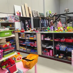Speelgoedafdeling in kringloopwinkel met dozen, bakjes en rekken vol speelgoed en kinderartikelen