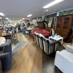 Winkelvloer van kringloopwinkel met diverse meubels: rode bank, gestreepte fauteuil, houten kast en andere tweedehandsartikel