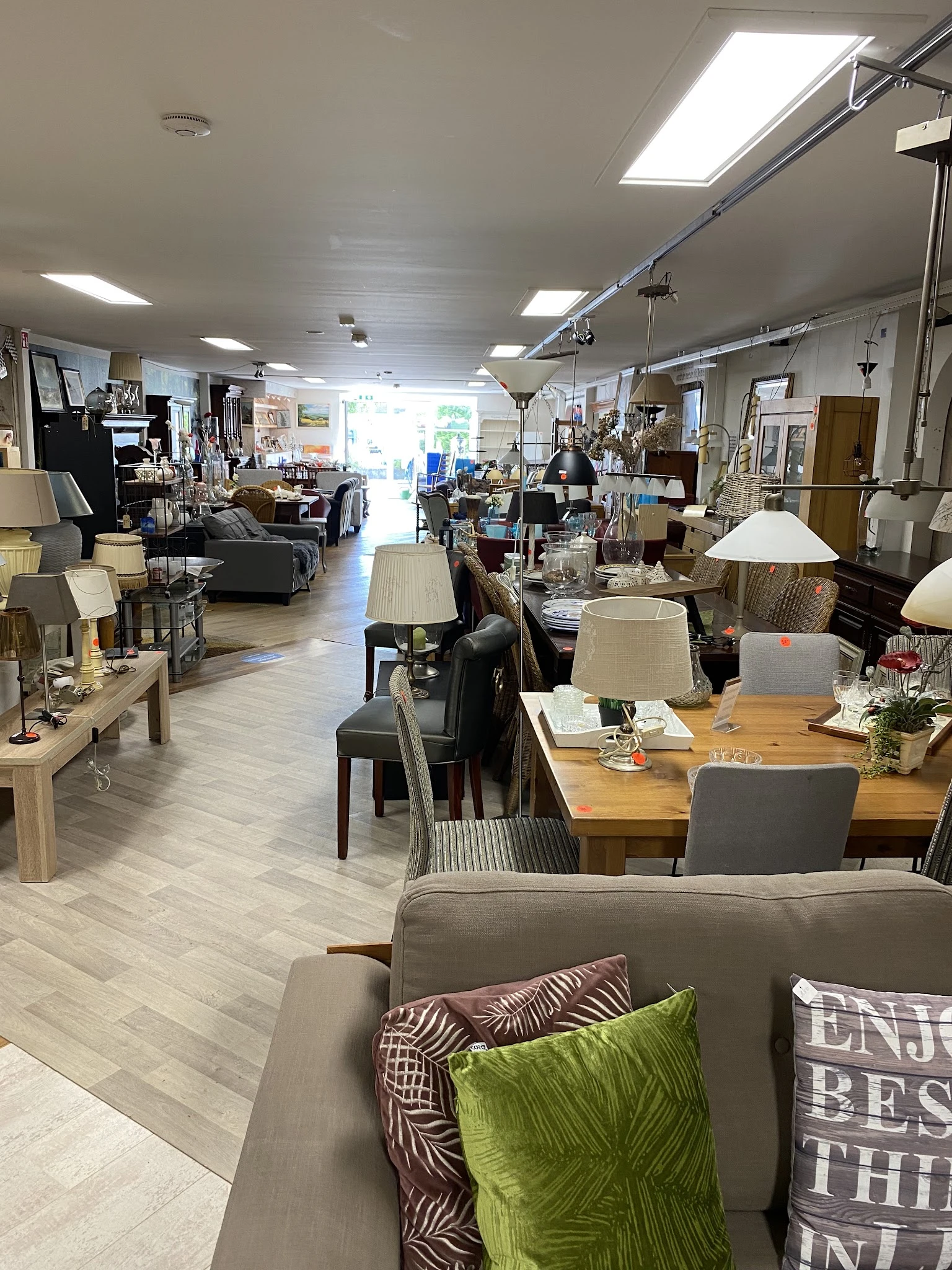 Binnenaanzicht van kringloopwinkel met diverse meubels, lampen, tafels en stoelen uitgestald op houten vloer