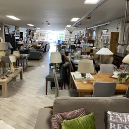 Binnenaanzicht van kringloopwinkel met diverse meubels, lampen, tafels en stoelen uitgestald op houten vloer