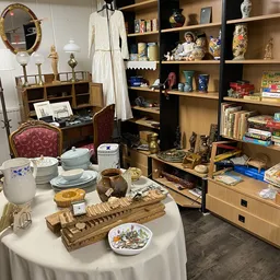 Uitstalling van diverse huishoudelijke artikelen: servies, bestek, houten snijplanken, decoratieve items en boeken in kasten 