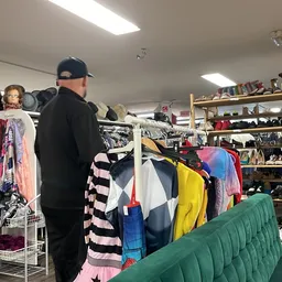 Winkelvloer van kringloopwinkel met kledingrekken, stellingen met diverse spullen en bezoekers aan het winkelen
