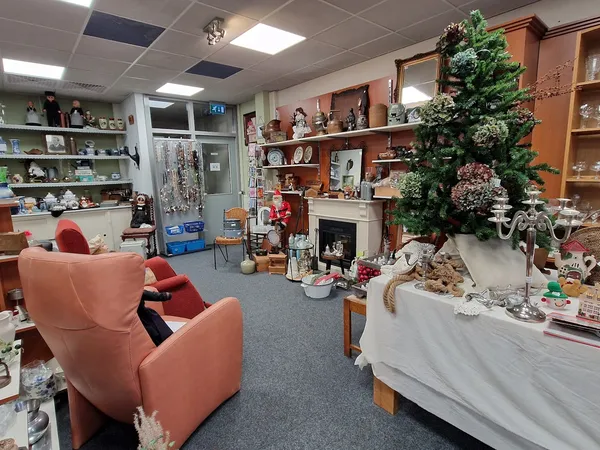 Winkelvloer met rode fauteuils, houten stellingen met decoraties, kunstplant en witte tafel met diverse spullen