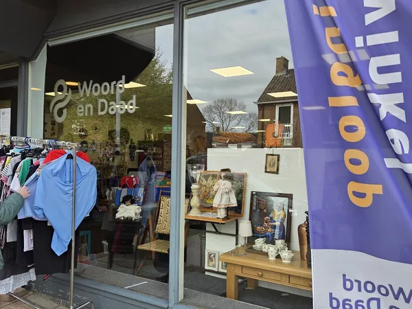Winkelruit met logo 'Woord en Daad' en uitstallingen met kleding en gebruiksartikelen