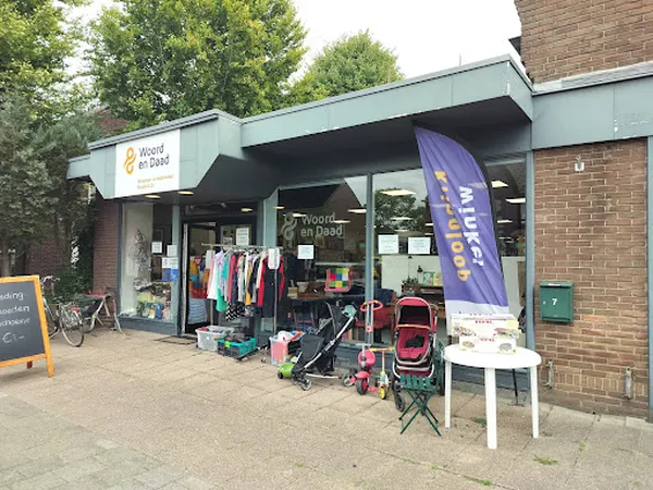 Gevel van kringloopwinkel met lichtblauwe pui, etalage met kleding, kinderwagens en spullen buiten uitgestald