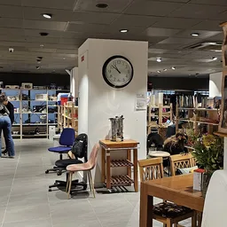 Winkelvloer van kringloopwinkel met houten meubels, stellingen, klok aan muur en bezoekers