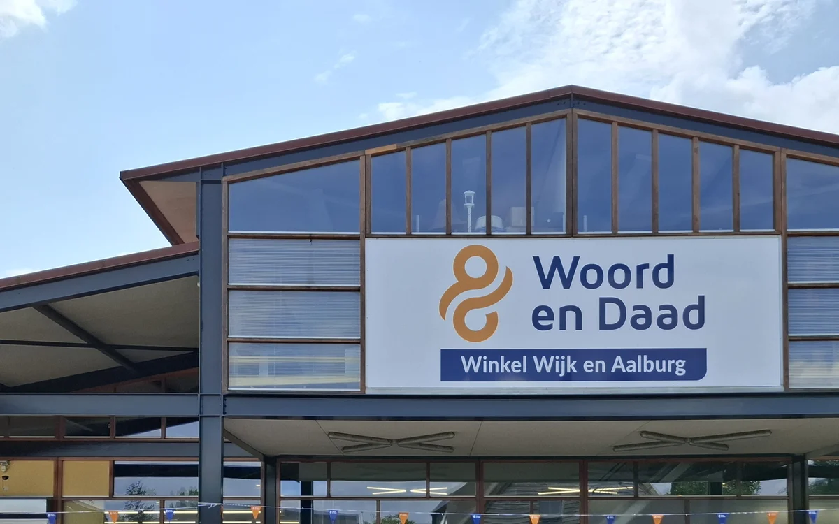 Moderne gevel van kringloopwinkel met groot logo en winkelnaam op wit paneel
