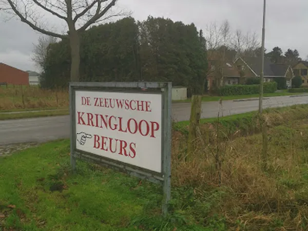 Wegbord met witte achtergrond en rode tekst 'DE ZEEUWSCHE KRINGLOOP BEURS' langs een landweg met huizen op de achtergrond