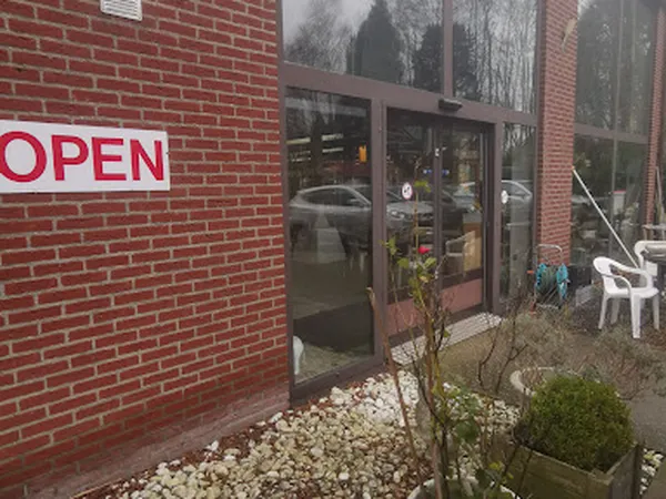 Bakstenen gevel van kringloopwinkel met rode 'OPEN' bord en glazen deur met zicht op interieur