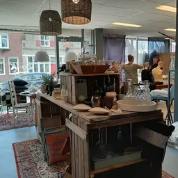 Winkelvloer van kringloopwinkel met houten meubels, hangende lampen en ramen met uitzicht op straat
