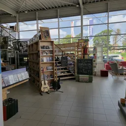 Ruim interieur van kringloopwinkel met stellingen, meubels en spullen verspreid over de vloer, grote ramen met uitzicht op st