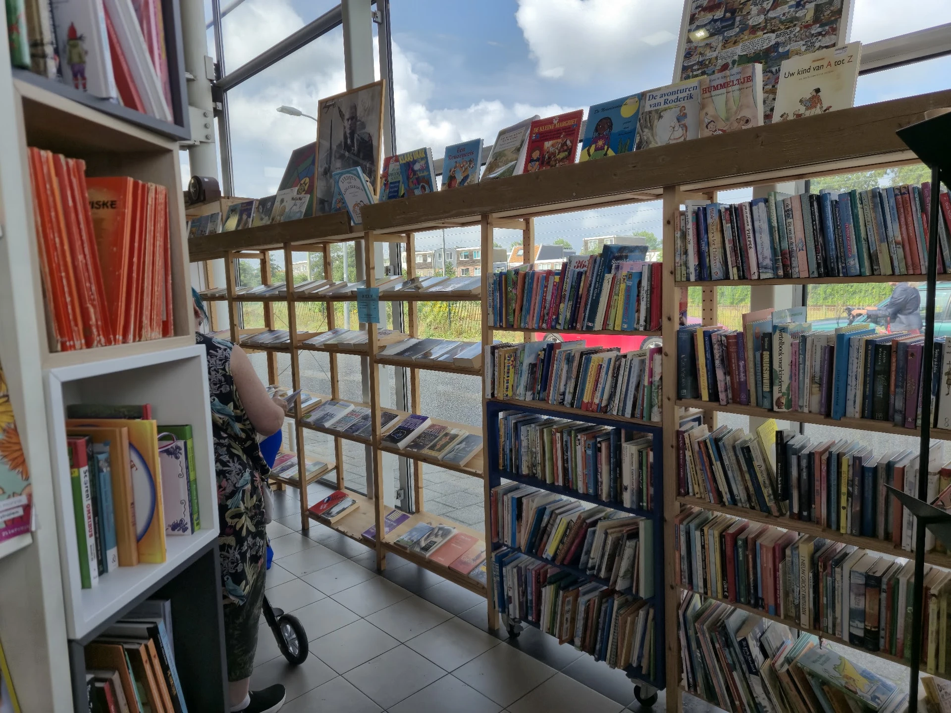 Binnenkant van kringloopwinkel met houten stellingen vol DVD's, CD's en boeken, natuurlijk licht van grote ramen