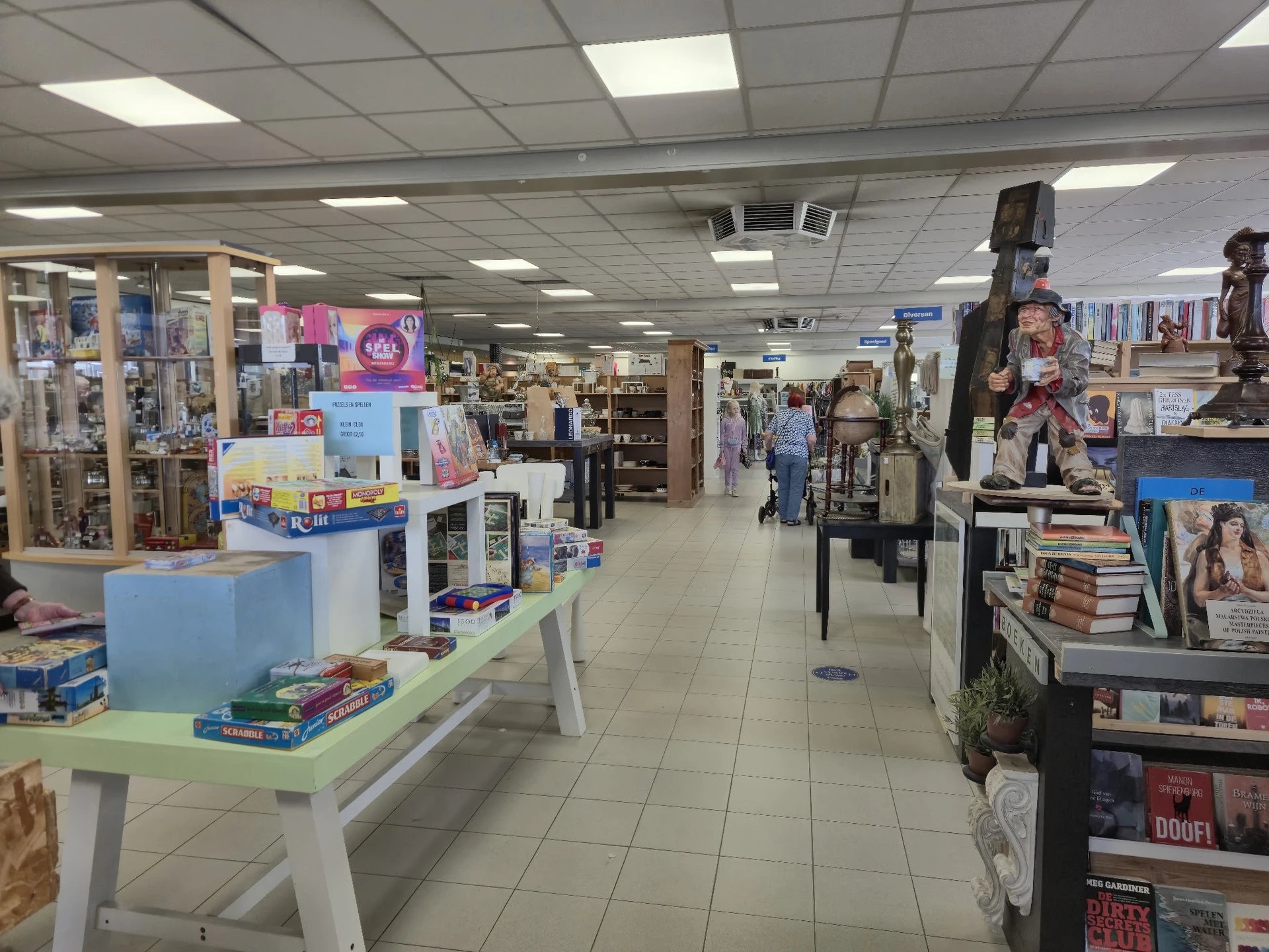 Winkelvloer van kringloopwinkel met stellingen, toonbanken en diverse tweedehands artikelen zoals boeken en kleding